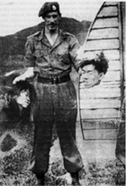 British Royal Marine in April 1952 grinning as he holds the severed heads of a young man and woman accused of supporting the Communist Party of Malaya