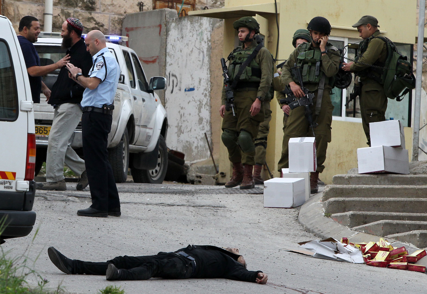 EDITORS NOTE: Graphic content / Israeli soldiers and police surround the body of one of two Palestinians who were killed after wounding an Israeli soldier in a knife attack before being shot dead by troops, an army spokeswoman said, at the entrance to the heavily guarded Jewish settler enclave of Tal Rumeda in the city centre of the West Bank town of Hebron on March 24, 2016. An Israeli soldier was detained after allegedly shooting a wounded Palestinian assailant in the head and killing him as he lay on the ground, the army said. In the video released by B'Tselem, an Israeli rights non-governmental organisation, the soldier appears to shoot the Palestinian again in the head without provocation as he lay wounded from a gun shot wound on the ground.    / AFP / HAZEM BADER        (Photo credit should read HAZEM BADER/AFP/Getty Images)